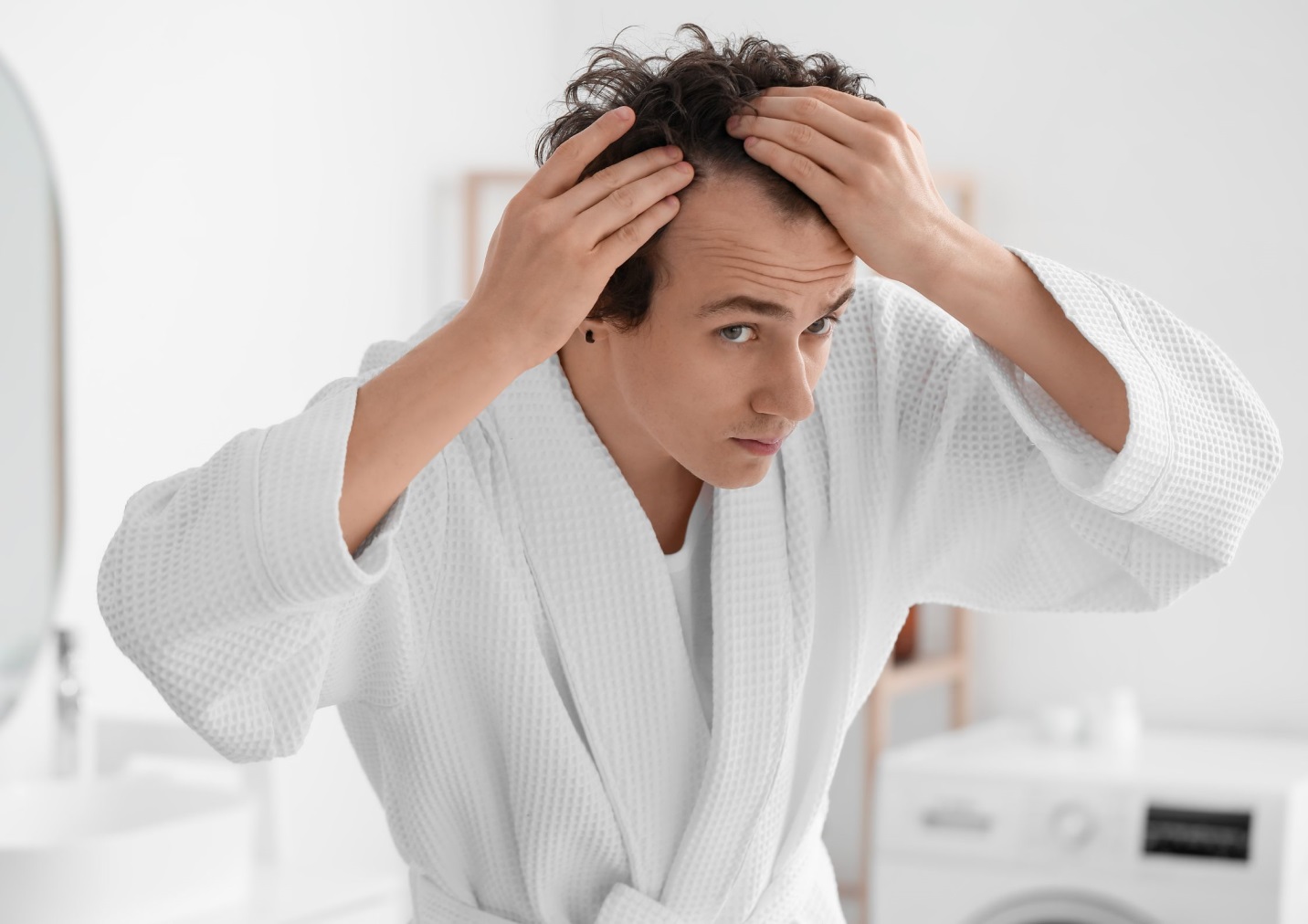 A person in a white robe touching his hair  Description automatically generated