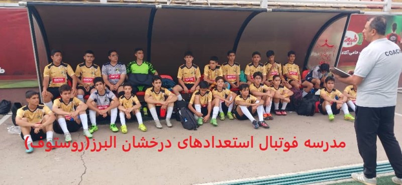 فوتبالیستهای نوجوان باشگاه فوتبال استعدادهای درخشان البرز(روستوف)با لباسهی طلایی نشسته روی نیمکت کنار زمین چمن فوتبال و گوش دادن به حرف مربی خود